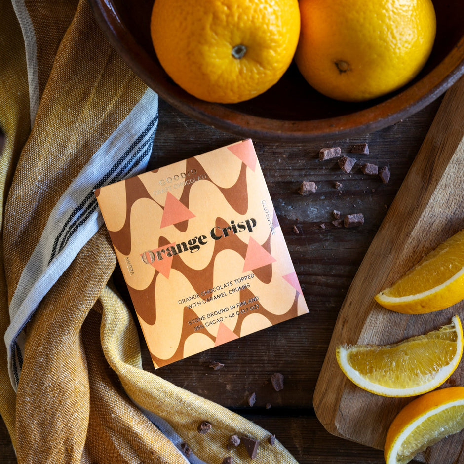 Bowl of oranges with Goodio Orange Crisp chocolate on a wooden surface.