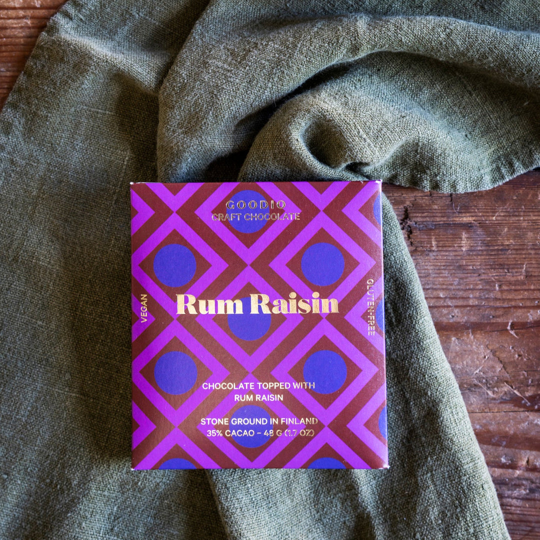 Purple and gold box of Rum Raisin chocolate on a textured green fabric background