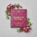 Lataa kuva gallerian katseluohjelmaan, A square package of Goodio Craft Chocolate Cranberry & Rosemary flavor, featuring a vibrant magenta and green patterned design with gold lettering, centered on a plain white background.
